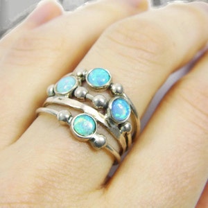 May include: A silver ring set with multiple bands, each adorned with small, round, light blue opal stones. The ring has a layered design with a cluster of opals on top.