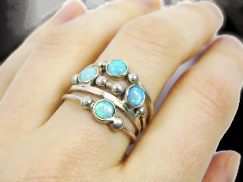 May include: A silver ring set with multiple bands, each adorned with small, round, light blue opal stones. The ring has a layered design with a cluster of opals on top.