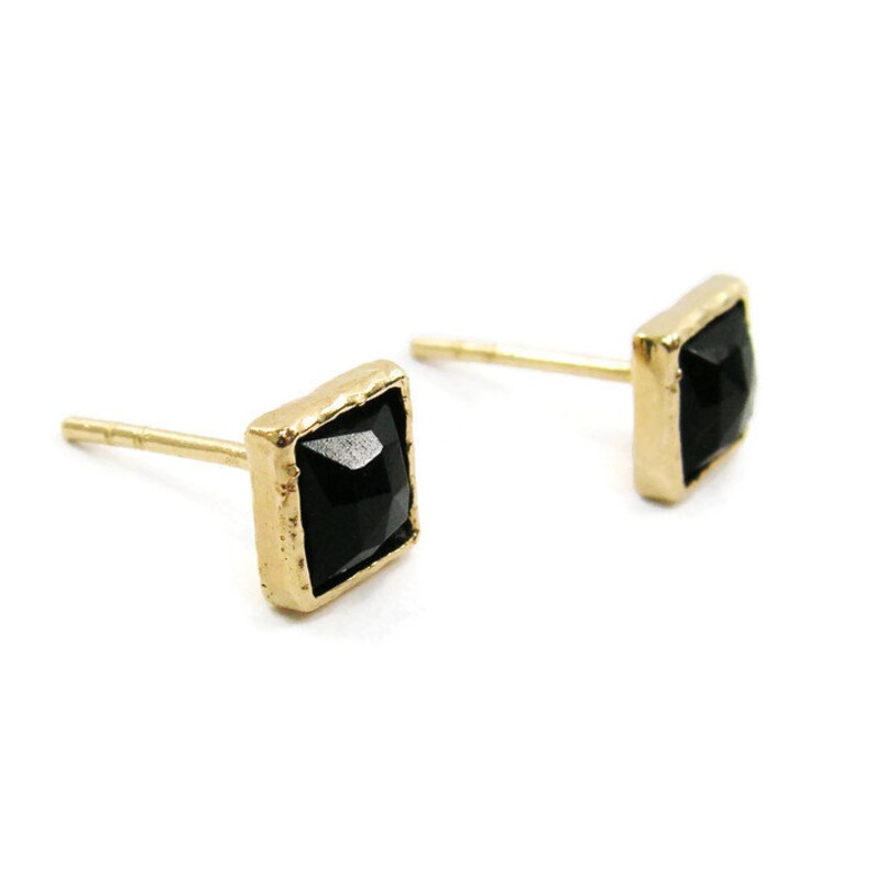 May include: A pair of gold earrings with black square-shaped gemstones.