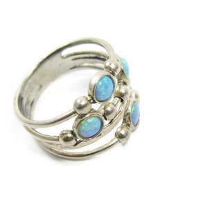 May include: A silver ring with multiple bands and small, round accents. The ring features several oval-shaped, light blue opal stones. The design is intricate and detailed, showcasing a vintage or handcrafted style. The ring is set against a white background.
