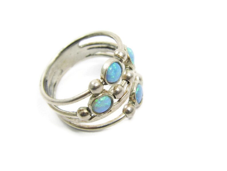 May include: A silver ring with multiple bands and small, round accents. The ring features several oval-shaped, light blue opal stones. The design is intricate and detailed, showcasing a vintage or handcrafted style. The ring is set against a white background.