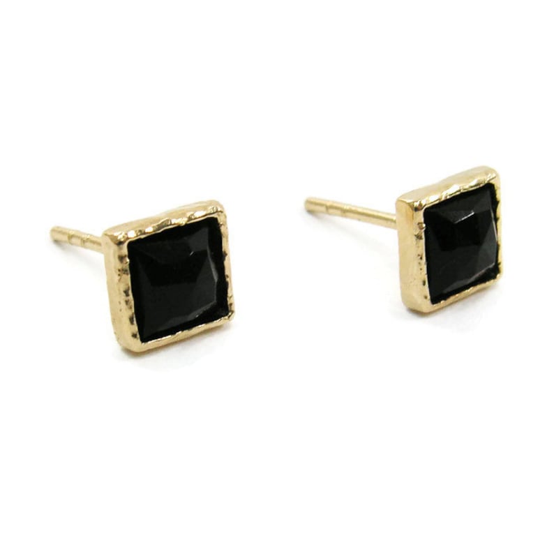 May include: A pair of gold square stud earrings with black gemstone accents.