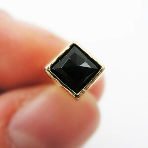 May include: A gold-toned earring with a black diamond-shaped gemstone.