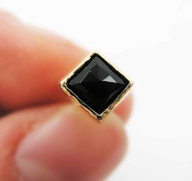 May include: A gold-toned earring with a black diamond-shaped gemstone.