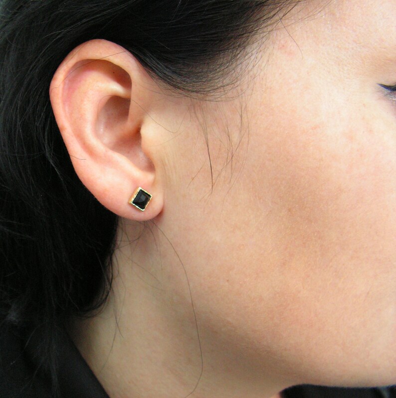May include: A pair of small, square-shaped earrings with black gemstones set in gold.