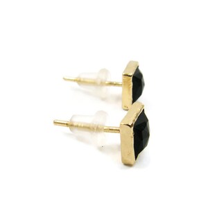 May include: A pair of gold stud earrings with black square-shaped gemstones.