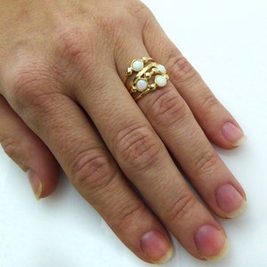 Puede incluir: Un anillo dorado con un dise&ntilde;o multicapa. El anillo presenta tres bandas con peque&ntilde;as piedras preciosas blancas y redondas. El anillo se lleva en un dedo, mostrando sus intrincados detalles y su estilo elegante.