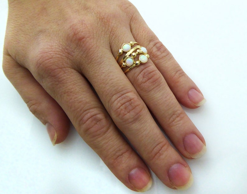 Puede incluir: Un anillo dorado con un dise&ntilde;o multicapa. El anillo presenta tres bandas con peque&ntilde;as piedras preciosas blancas y redondas. El anillo se lleva en un dedo, mostrando sus intrincados detalles y su estilo elegante.