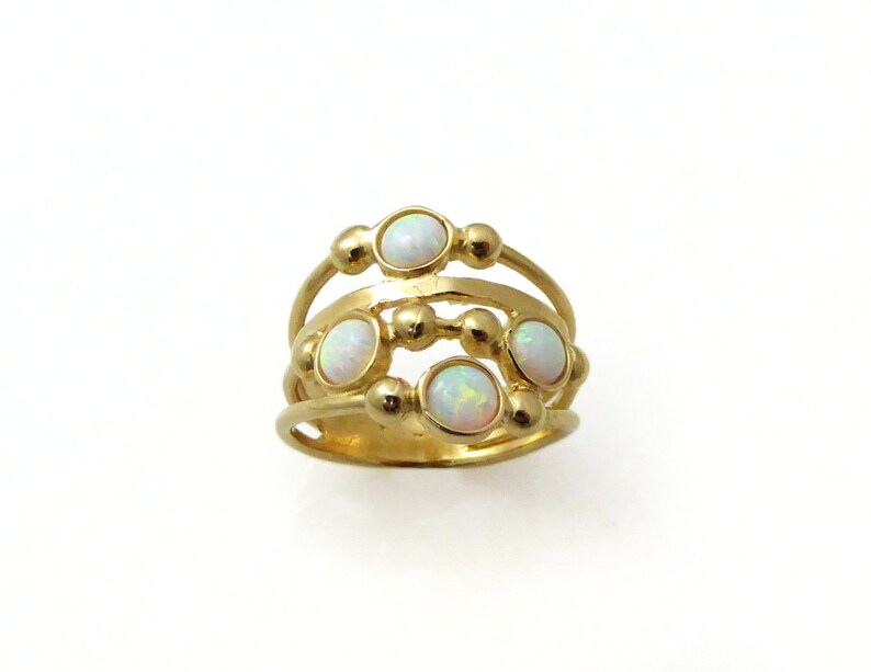 Puede incluir: Un anillo dorado con m&uacute;ltiples bandas y peque&ntilde;as piedras de &oacute;palo redondas. El anillo tiene un dise&ntilde;o &uacute;nico con una apariencia en capas, que combina texturas lisas y con cuentas. Los &oacute;palos son ovalados y est&aacute;n engastados en la banda dorada.