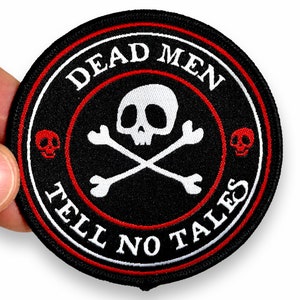 May include: A round, black embroidered patch with the text "DEAD MEN TELL NO TALES" in white. The patch features a white skull and crossbones in the center, with red skull accents and a red and white border.