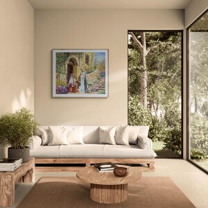 May include: A living room with a framed painting depicting figures near a stone building. A white sofa with pillows, a wooden coffee table, and a small side table with a plant are in the foreground. A large window offers a view of trees.