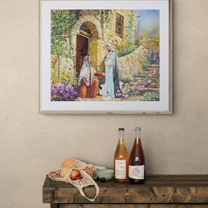 May include: A framed painting depicts a biblical scene with two figures in front of a stone building with an arched doorway. Below, a wooden table displays two wine bottles, a string bag with fruit, and a small bowl.