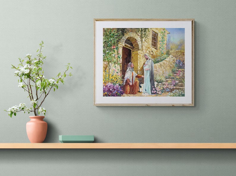 May include: A framed print depicting a religious scene with two figures in a garden setting. The artwork features a stone building with an arched doorway, lush greenery, and colorful flowers. The print is displayed on a light-colored wooden shelf.