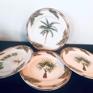 May include: A set of ceramic plates with a tropical theme. Each plate features a palm tree design in the center, surrounded by green palm fronds and a brown bamboo-style border. The plates are white and tan.