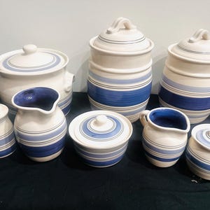 May include: A set of three ceramic mugs with a speckled, matte finish. The mugs are in shades of cream, light grey, and dark grey. Each mug has a simple, minimalist design and a rounded handle. The mugs are stacked on top of each other.