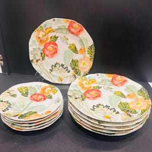 May include: A collection of ceramic plates with a floral design. The plates have a white base adorned with watercolour-style illustrations of red and orange flowers, green leaves, and small yellow details. The plates are in different sizes and shapes.