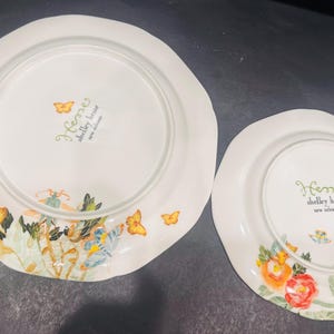 May include: Two white ceramic plates with scalloped edges. The plates are decorated with colourful floral and butterfly designs. The text "Heme shelley house new release" is printed on the plates.