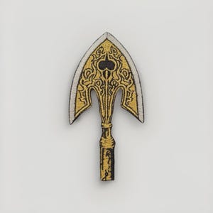 May include: Embroidered patch in the shape of an ornate arrow. The patch features gold and black thread detailing on a white background. The arrow design has a stylized, decorative pattern.