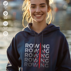 May include: A navy blue hoodie featuring the word "ROWING" repeated five times in a stacked design. A red rowing oar graphic is centered on the right side of the text. The hoodie is a cotton blend and is machine washable.