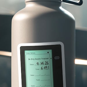 May include: A gray water bottle with a black handle and a digital display. The display shows "2k Erg Score Tracker" with a date of 9/14/26 and a time of 6.491. The bottle is cylindrical and appears to be made of metal.