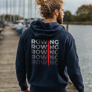 Puede incluir: Sudadera con capucha azul marino con la palabra "ROWING" impresa en un diseño apilado en la espalda. La palabra está en una fuente gris con una línea vertical roja. La sudadera tiene una capucha con cordón.