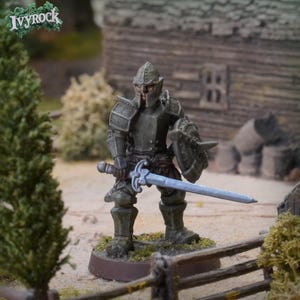 Puede incluir: Figura de caballero en miniatura con armadura completa, sosteniendo una espada y un escudo. El caballero está pintado en tonos grises y marrones, con un casco y una armadura detallados. La figura se encuentra sobre una base marrón, con un fondo borroso.