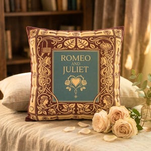 May include: A decorative square pillow featuring the text "Romeo and Juliet" in a teal rectangle, surrounded by ornate gold and burgundy designs. The pillow has a burgundy border and is resting on a bed with a neutral-colored pillow.