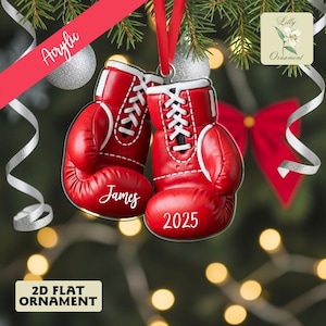 May include: A red acrylic Christmas ornament shaped like a pair of boxing gloves. The gloves have white laces and trim, with the name "James" and the year "2025" printed on them. The ornament hangs from a red ribbon.