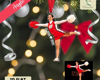 May include: Acrylic 2D flat ornament featuring a cheerleader in a red and white uniform, holding red and white pom-poms. The ornament has the name "ALISSA" and the year "2025" printed on it. The ornament is hanging from a red ribbon.