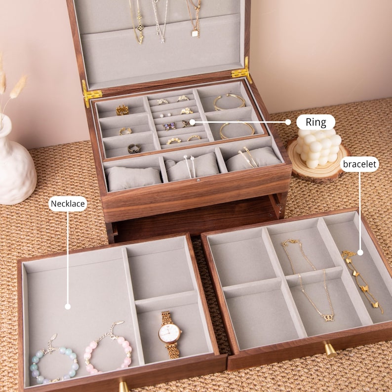 May include: A wooden jewelry box with multiple compartments, including sections for rings, bracelets, and necklaces. The box is open, revealing various pieces of jewelry. The interior is lined with gray fabric, and the box has a warm, natural wood finish.