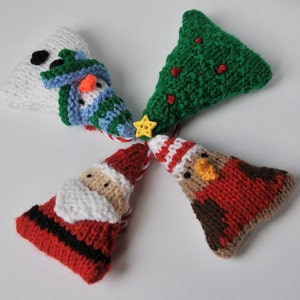 Op de afbeelding: Een verzameling van vier gebreide kerstversieringen. De ornamenten omvatten een sneeuwpop, een kerstboom, de kerstman en een roodborstje. De ornamenten zijn gemaakt van garen in verschillende kleuren, waaronder wit, groen, rood en bruin.
