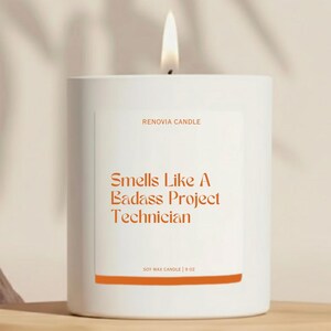 May include: A white soy wax candle with a lit wick. The label reads "Smells Like A Badass Project Technician" in orange text. The candle is 9 oz.