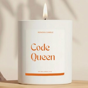 May include: A lit white candle with the text "Code Queen" in orange. The candle is in a white cylindrical container with a label that reads "RENOVIA CANDLE" and "SOY WAX CANDLE | 9 OZ". The candle sits on a wooden shelf.