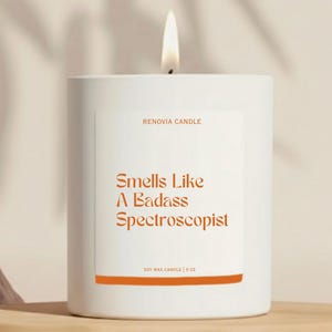 May include: A white soy wax candle with a lit wick. The label reads "RENOVIA CANDLE" and "Smells Like A Badass Spectroscopist" in orange text. The bottom of the label says "SOY WAX CANDLE | 9 OZ".