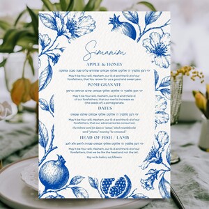 May include: A rectangular card featuring a blue and white botanical illustration of flowers and pomegranates. The text reads Simanim, Apple & Honey, Pomegranate, Dates, and Head of Fish / Lamb, accompanied by traditional prayers in Hebrew and English.