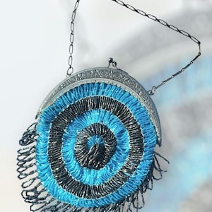 May include: A vintage-style purse with a silver-toned frame and chain handle. The circular body features concentric circles of blue and black beads, with a beaded fringe along the bottom edge. The purse has a clasp closure.