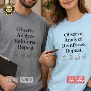 Könnte beinhalten: Ein graues T-Shirt und ein hellblaues T-Shirt, jeweils mit dem schwarzen Text Observe, Analyze, Reinforce, Repeat. Unter dem Text befinden sich vier Symbole: ein Klemmbrett, eine Liste, ein Balkendiagramm und ein Haken in einem Kreis, mit kleinen Punkten.