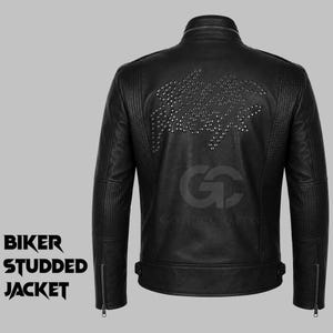 Könnte beinhalten: Eine schwarze Bikerjacke aus Leder mit Stehkragen, gerippten Schulter- und Ärmelpartien sowie silberfarbenen Metallnieten in Schriftzug-Optik auf dem Rücken. Die Jacke verfügt über Reißverschlüsse an den Ärmelbündchen und seitliche Verstellriemen.