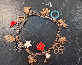 May include: A gold-colored charm bracelet with various charms, including a red heart, a black cat, a white star, a red flower, and an elephant. The bracelet also features a blue ring and a charm that says "Created for you."