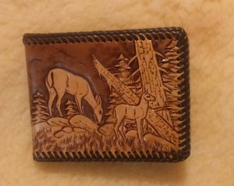 May include: A brown leather wallet with a tooled design of two deer in a forest setting. The wallet has a dark brown stitched border.