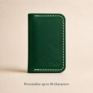 Puede incluir: Un tarjetero de cuero verde oscuro con costuras de color claro a lo largo de los bordes y la palabra Dude grabada en la esquina inferior derecha. El texto debajo del tarjetero dice Personalize up to 10 characters.