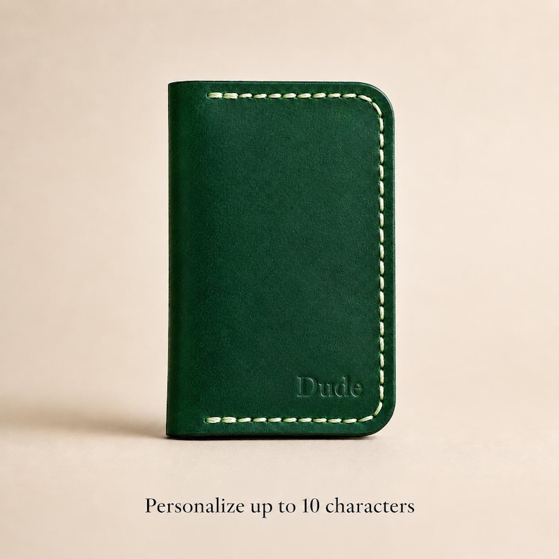 Puede incluir: Un tarjetero de cuero verde oscuro con costuras de color claro a lo largo de los bordes y la palabra Dude grabada en la esquina inferior derecha. El texto debajo del tarjetero dice Personalize up to 10 characters.