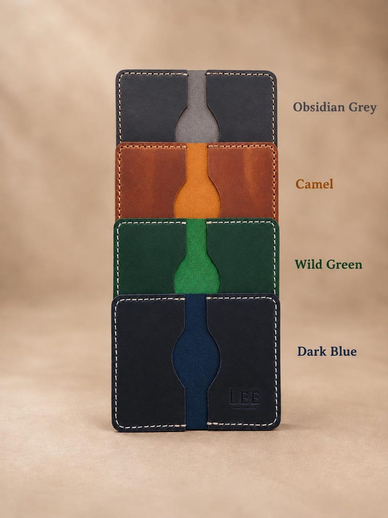 Puede incluir: Una pila de cuatro tarjeteros rectangulares en gris obsidiana, camel, verde salvaje y azul oscuro. Cada tarjetero presenta una muesca central para el pulgar y costuras blancas en contraste. El tarjetero azul oscuro tiene el texto LEE.