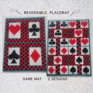 May include: A reversible rectangular placemat featuring two distinct sides with a red and black checkered border. One side displays four large playing card suit symbols in white panels, while the other side features a grid of smaller suit icons.