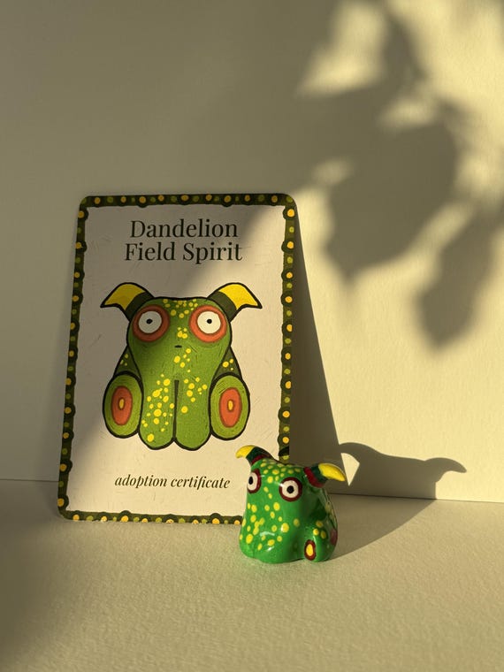 A hand-sculpted goblincore clay spirit with a dandelion theme and a tiny adoption certificate — that certificate detail pushes this from cute to genuinely charming.