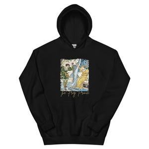 May include: Black hooded sweatshirt featuring a colorful illustration of a scene with two figures and the text "The Frog Prince" in gold script. The artwork depicts a man in green and a woman in a yellow dress.