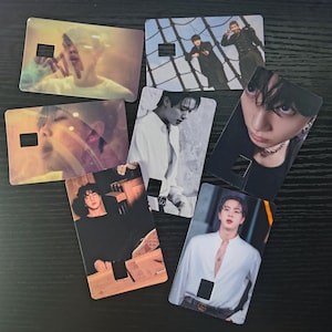May include: A collection of seven rectangular cards featuring images of people. Each card has a rectangular cutout near the top and is printed with a different photograph. The cards are arranged on a dark surface.
