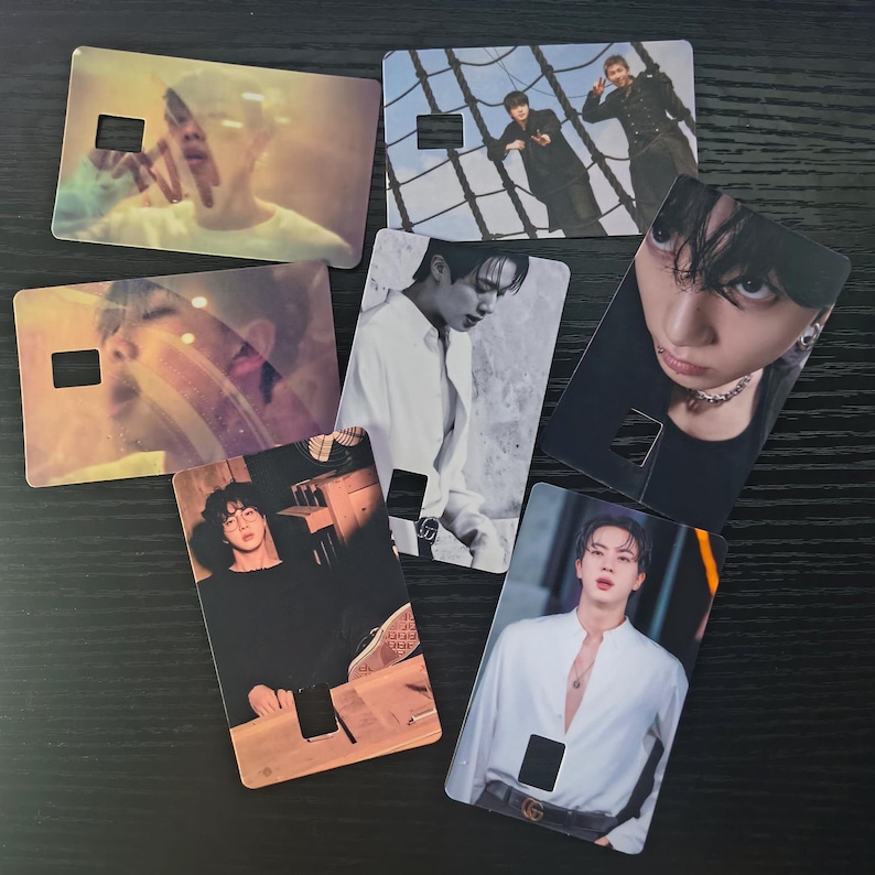 May include: A collection of seven rectangular cards featuring images of people. Each card has a rectangular cutout near the top and is printed with a different photograph. The cards are arranged on a dark surface.