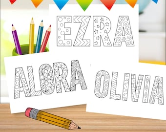 May include: Three white cards with the names "EZRA", "ALORA", and "OLIVIA" in black, decorative fonts, ready for coloring. A pencil and a green cup with colored pencils are on a wooden surface. Colorful pennant banner in the background.
