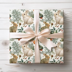 May include: A wrapped gift with a cream satin ribbon. The wrapping paper displays a repeating pattern of watercolour bunnies, pine branches, holly, and pine cones on a white background. The design has a festive, seasonal theme.